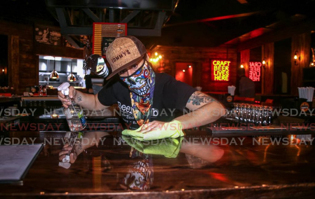 Barman Andrea Roass cleans the counter of Tommy's Bar in MovieTowne, Port of Spain in preparation for the opening of safe zones next Monday. PHOTO BY SUREASH CHOLAI - 