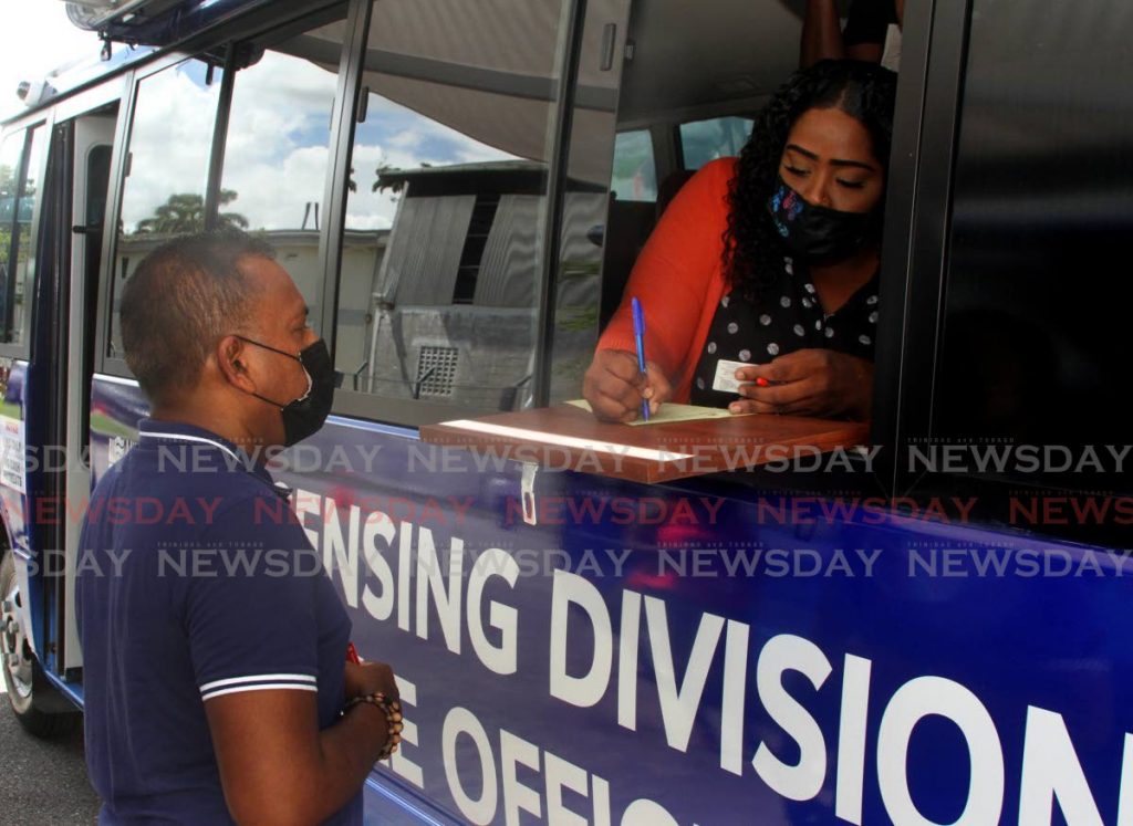 Shiva Lakhan is attended to by Licensing Division mobile office electronic processing officer Christion Griffith at the launch of the service at the Caroni Licensing Office on Tuesday. - Photo by Angelo Marcelle