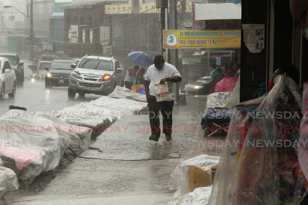 A man walks briskly to heavy rainfall on High Street, San Fernando on Tuesday. TT is under a tropical wave alert until Saturday. - Photo by Marvin Hamilton