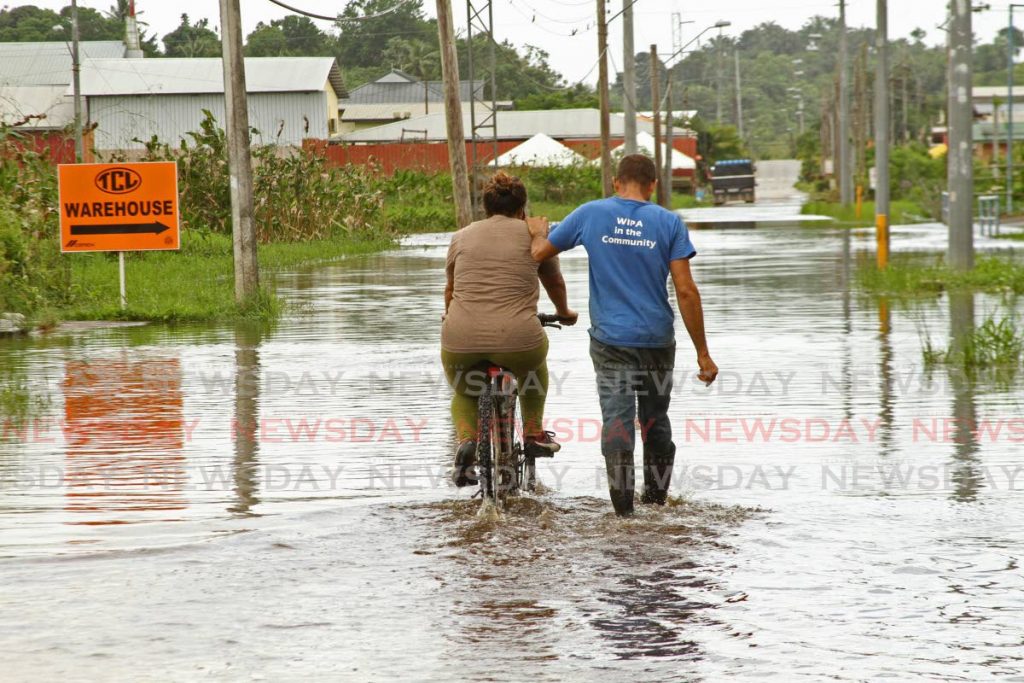 In this file photo, a man walks alongside a woman who rides a bicycle through flood waters in Katwaroo Branch Trace in Penal following heavy showers. -