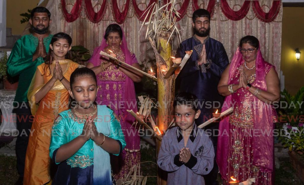 Tobago Hindu Society president Pulwaty Beepath, back centre, and her family pray after lighting deyas at her home in Scarborough on Monday. - David Reid
