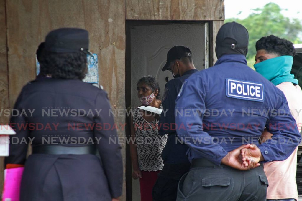 Police officers interview Myna Jagroop at her home on Monday after a relative killed two and wounded two during a chopping rampage on Sunday night. PHOTO BY MARVIN HAMILTON - 