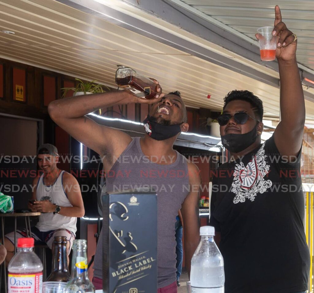 Trinidadian Dave Roopchan takes a shot of whisky straight from the bottle while liming with his friend Narad Ramnarine at Up Top Bar and Lounge, Crown Point on Thursday.  - Photo by David Reid