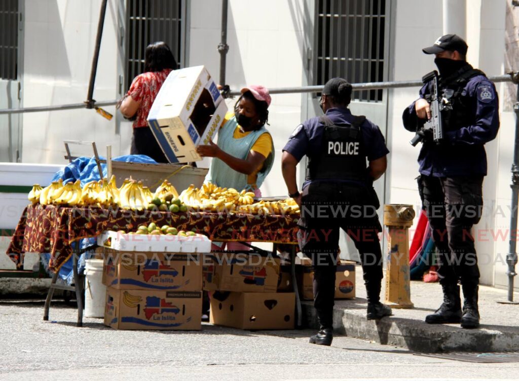 Municipal police officers of the Port of Spain City Corporation keep a close eye on a vendor who was industucted to pack up her goods for illegally vending along Henry Street, Port of Spain. - PHOTO BY AYANNA KINSALE