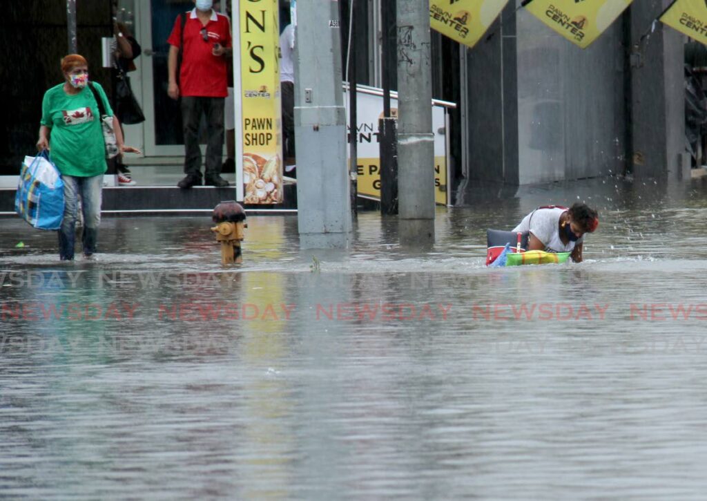 In this file photo, a woman tries to get up after falling in flood water while trying to cross South Quay, Port of Spain. - 