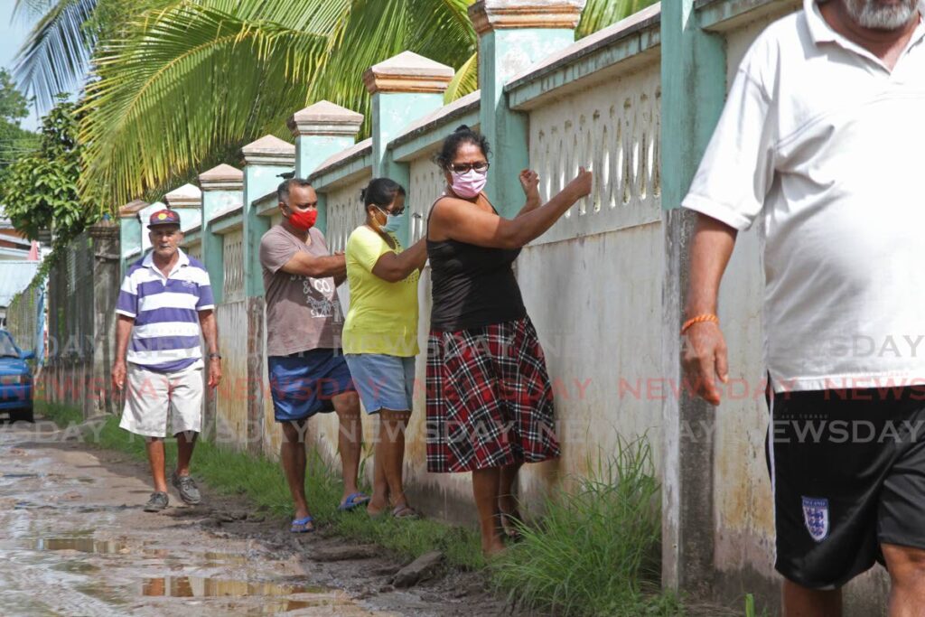 On Tuesday, residents of Deosaran Trace, San Francique Road, Penal demonstrated how they get in and out of the community when the street is flooded and the already bad road becomes impassable due to potholes by using the neighbor's fence for support. Photo by Marvin Hamilton