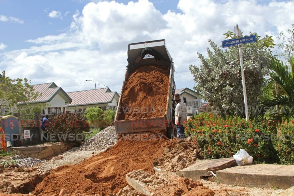 A contractor supervises a lorry operator as dirt is dumped on part of the excavated road at Oasis Gardens, Chaguanas on Wednesday.  - Marvin Hamilton