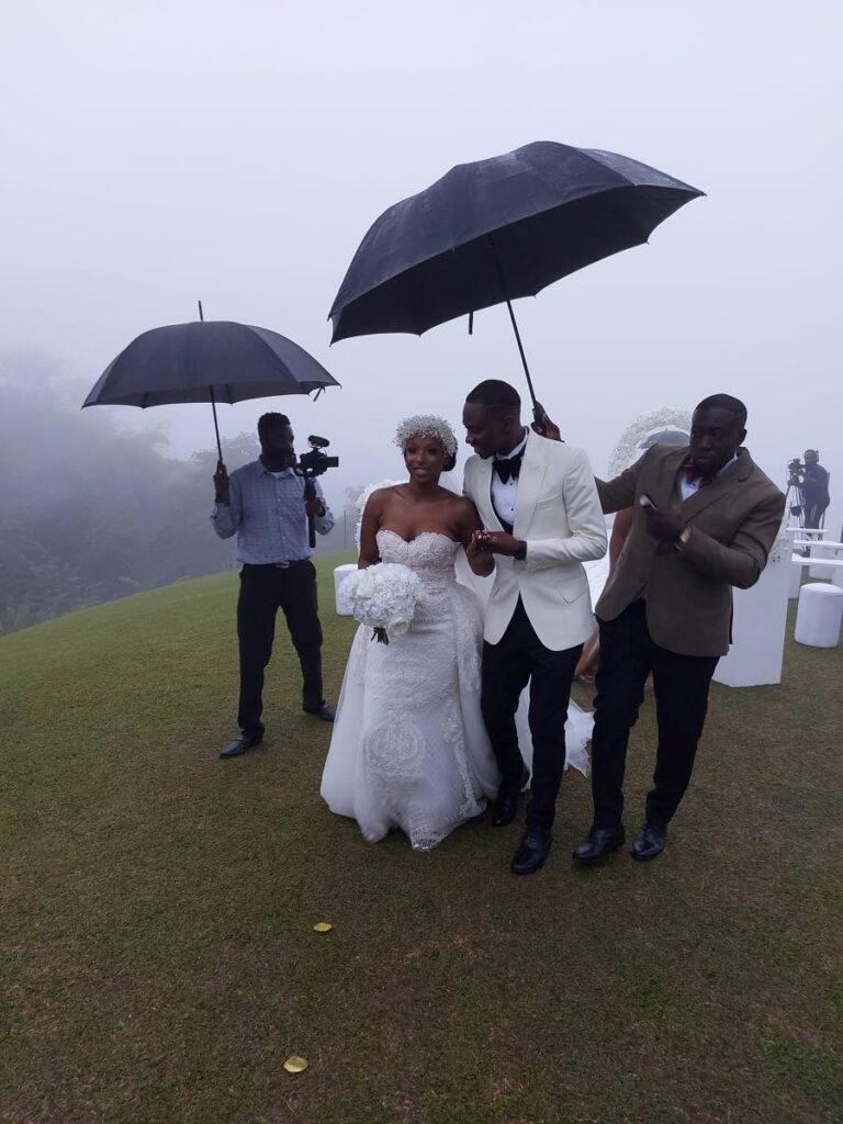 Chief Secretary Farley Augustine and his wiffe Takyana are sheltered from the rain as they leave Flagstaff Hill in Charlotteville where they exchanged vows on Sunday. - PHOTO COURTESY NEW LENS