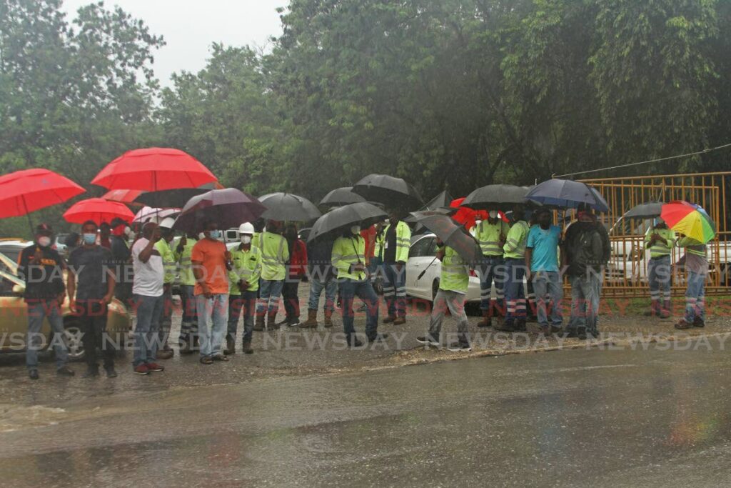 TCL workers brave the rains to demand answers from the company on the non-payment of COLA outside the plant in Savonetta on Wednesday. - Photo by Marvin Hamilton