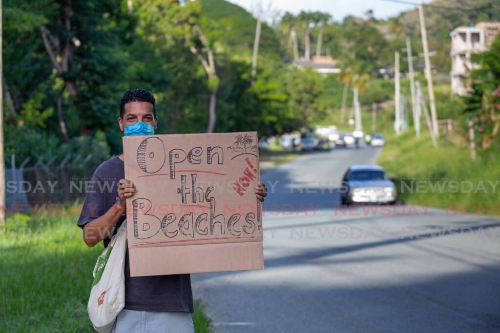 Mt Irvin resident Odilly Belgrave displays his “Open the Beaches” sign at Old Grange Bay on Wednesday where many beach operators planned a silent demonstration. - David Reid