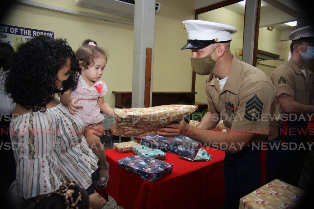 Gunnery Sgt Christopher Claspille  presents a gift to Emilyos Pinto, held by her mother Elaina Reyes, during a US Embassy TT Christmas toy drive for migrants at St Benedict's RC Church, La Romaine - Photo by Lincoln Holder
