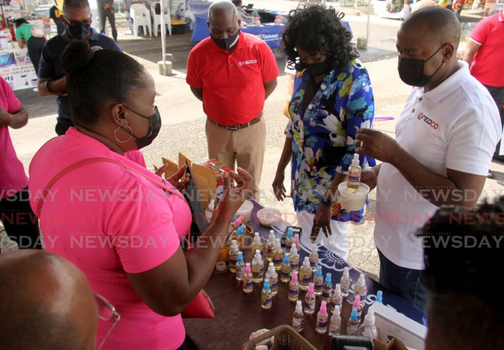 Maureen Pierre-John, of Karrah Kare, explains to Minister of Youth Development and National Service Foster Cummings and Minister of Social Development and Family Services Donna Cox the benefits of the products at the Nedco-sponsored Christmas Village, Queen's Park Savannah, Port of Spain. Also in the photo is Nedco CEO Calvin Maurice. 2021.12.18 - PHOTO BY AYANNA KINSALE