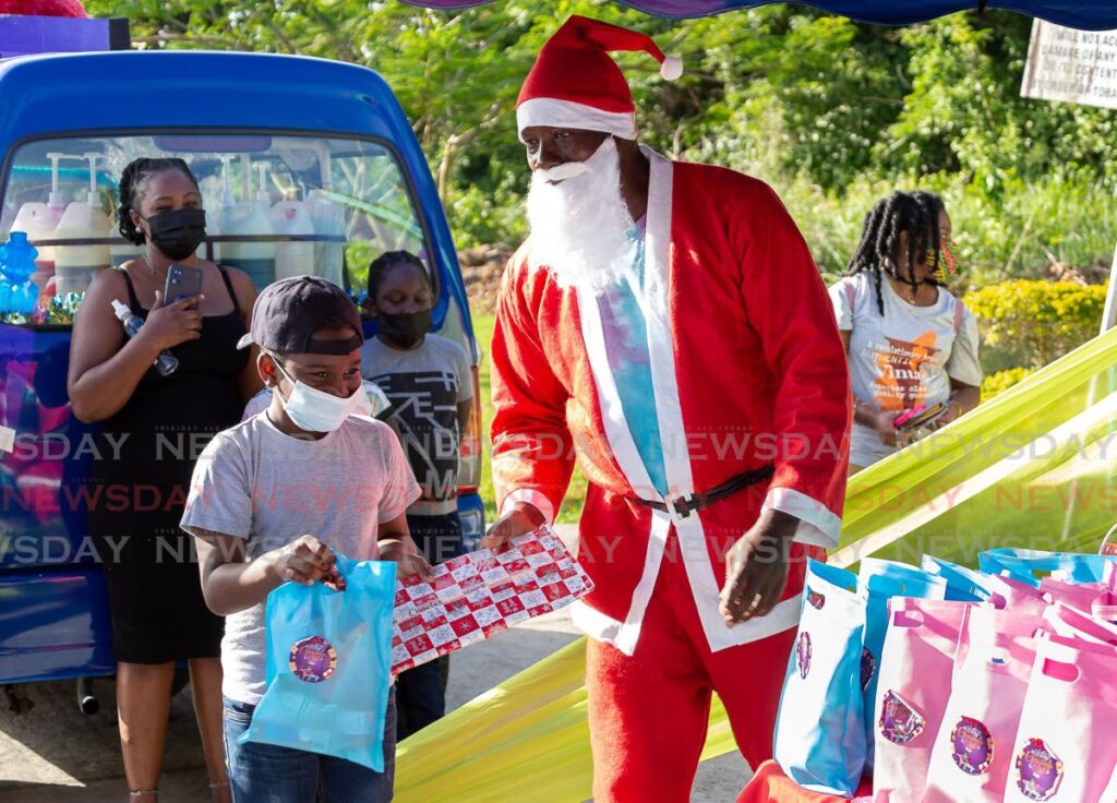 EARLY PRESENT: Izaiah Charles, left, collects his Christmas gift from Santa Claus, portrayed by Michael Frank of Frankie Reef Boat Tours, at Toya’s Couture second annual Christmas function held at Mt Irvine beach car park on Sunday. Photo by David Reid