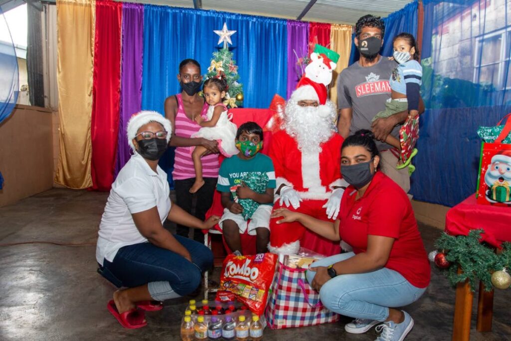 Digicel telesales agent, Andrea Inniss, right, during a distribution of food hampers and presents to a family from Samaroo Village, Arima. - 