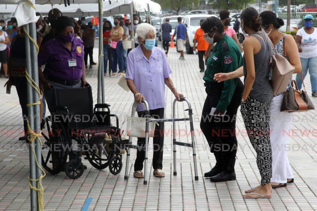 File photo: A woman is given a  wheelchair while she waits to be registered to have her vaccine booster at the SAPA mass vaccination site in San Fernando. Photo by Lincoln Holder