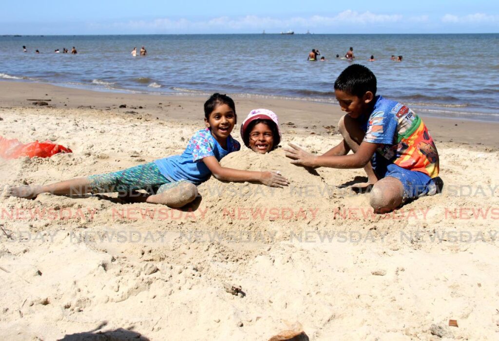 Siblings Rianna and Rishawn Jagroo cover their cousin Ishana Choon with sand at the Clifton Hill Beach in Point Fortin on Monday.  - AYANNA KINSALE