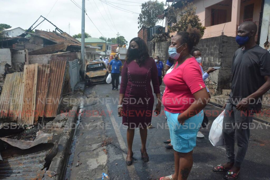 Minister Donna Cox looks at the damage done to the seven homes, with two of the fire victims on Quarry Street on Sunday. PHOTO COURTESY MINISTRY OF SOCIAL DEVELOPMENT - 