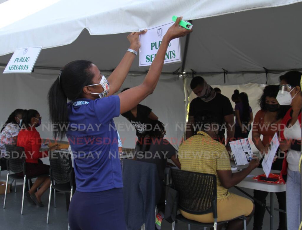 A health official places a public servants sign on a tent at the vaccination site at Southern Academy for the Performing Arts (SAPA), San Fernando.  Photo by Ayanna Kinsale