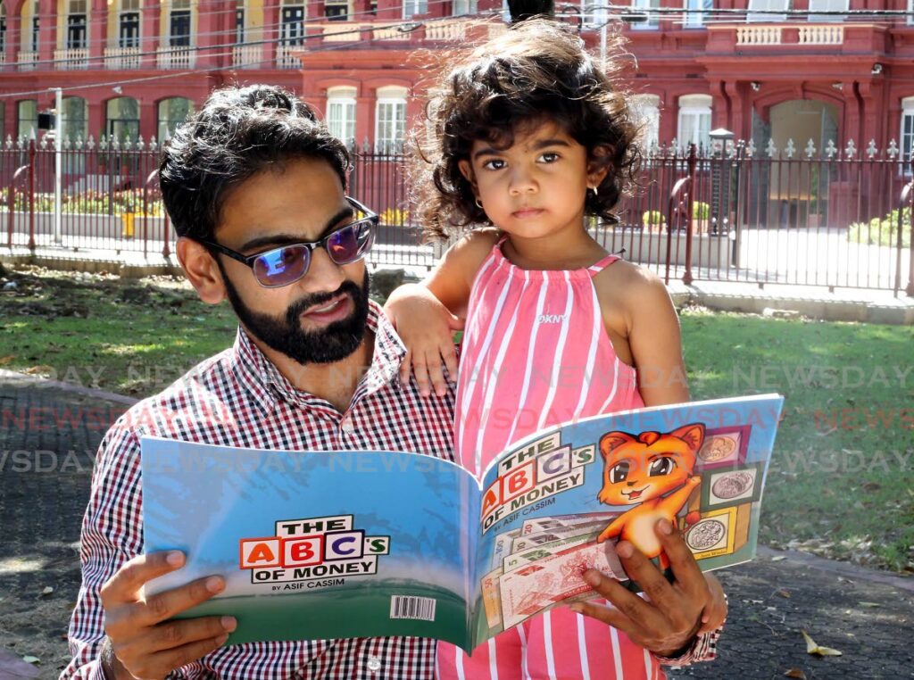 Author Asif Cassim holds his daughter, Raina  and his book The ABC's of Money. - ROGER JACOB
