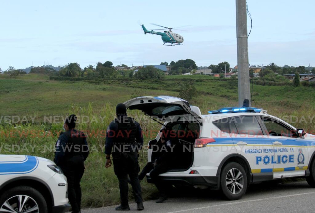 Police officers look on as a helicopter hovers over a field on the Solomon Hochoy Highway, Couva as they search for one of the suspects involved in a vehicle robbery which took place in Union Hall, San Fernando, on Monday. - AYANNA KINSALE