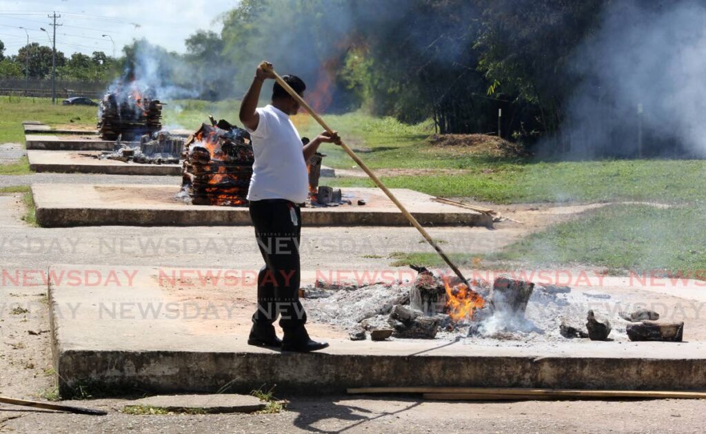 An attendant tends to a burnt funeral pyre of a non-covid victim at the Caroni Cremation Site, North Bank Road, Caroni on Friday. - ROGER JACOB
