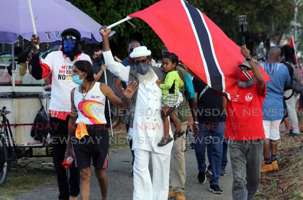 Umar Abdullah, leader of the First Wave Movement, carries a child as he and supporters walk around Queen’s Park Savannah, Port of Spain in an incident-free march on Saturday.  - SUREASH CHOLAI
