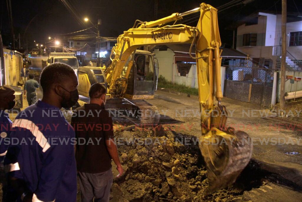 In this file photo, Ministry of Works and Transport workers look on as a machine operator uses an excavator to remove dirt from a hole as they begin work on the damaged road on the Southern Main Road in Claxton Bay. - Photo by Ayanna Kinsale