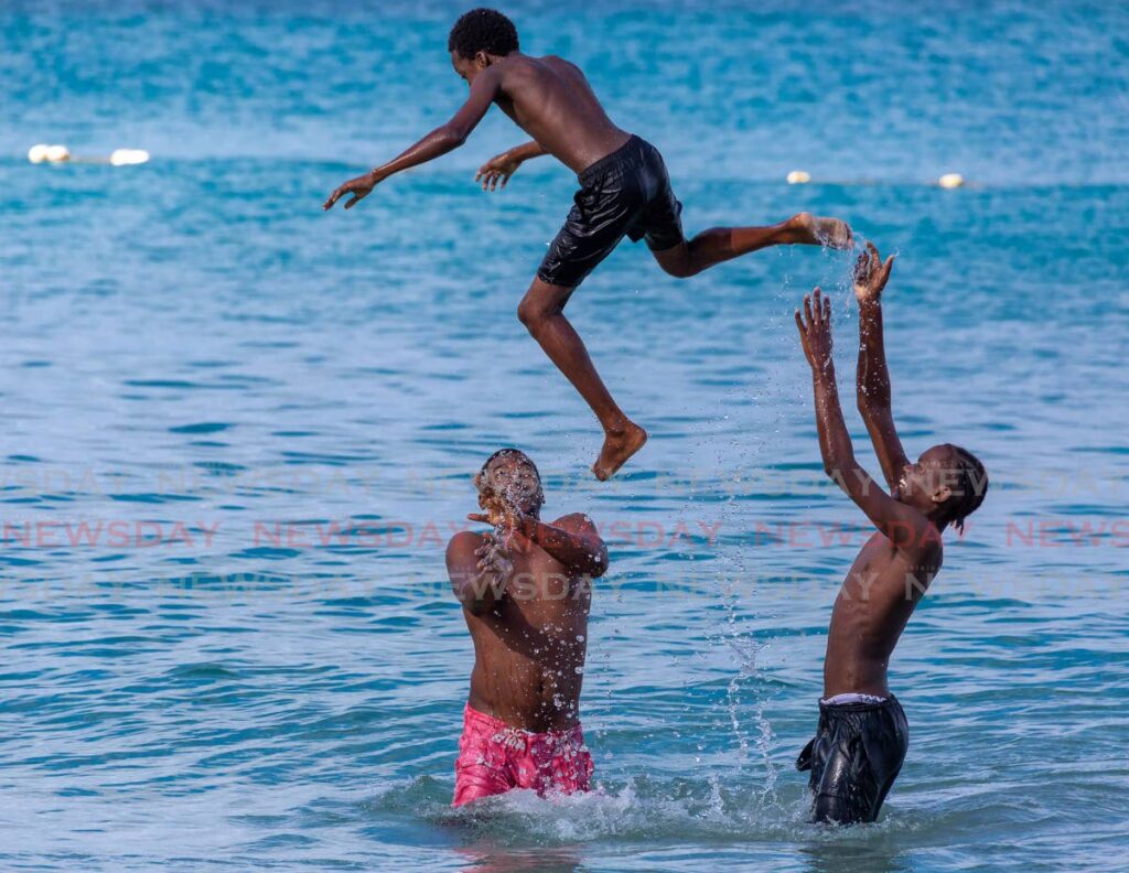 Terrell Monroe, left, and his nephew Terrell Lashley, right, throw Lashley's brother Tyrique into the air while having fun bathing at Store Bay, Tobago. Beaches and rivers will no longer have a 6 pm closing time from Monday. - File photo/David Reid