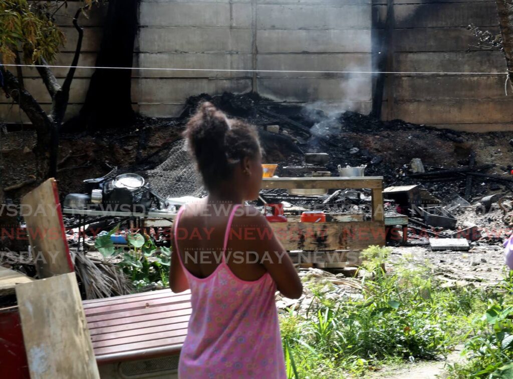 A neighbour looks at the smouldering remains of a house destroyed by fire at Phase 5, Beetham Gardens during a fight between two brothers on Tuesday morning. - SUREASH CHOLAI