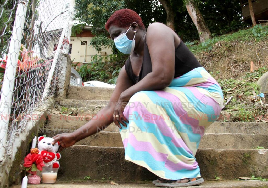 Sandra Spring places a teddy bear on the step where her relatives, Joseph Spring, Kevin Spring, and neighbour Randell John were shot and killed on Saturday night at Cemetery Street in Diego Martin. Another relative, Rawl Spring was taken to the hospital where he is still warded. - Photo by Ayanna Kinsale