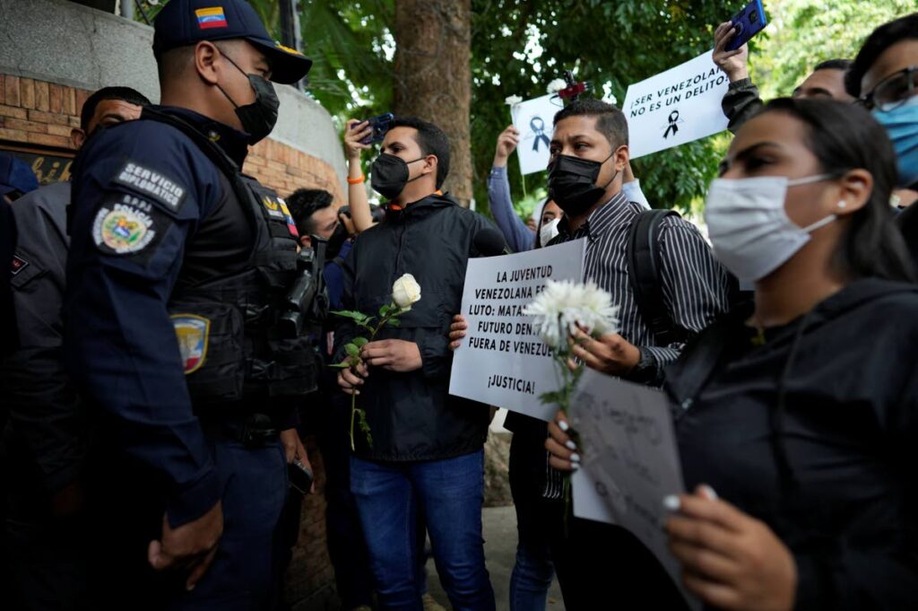 People holding signs and flowers protest against Trinidad and Tobago Coast Guard officers firing on a migrant boat, in front of the Trinidad and Tobago Embassy, in Caracas, Venezuela, Tuesday. AP PHOTO 