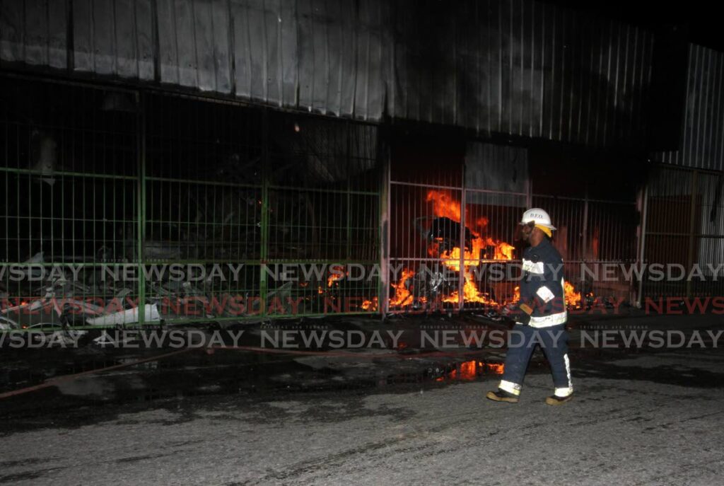 A fire officer walks past raging fire at D One Stop Auto Parts at Bamboo 2, Bamboo Village, on Monday night.  - Angelo Marcelle