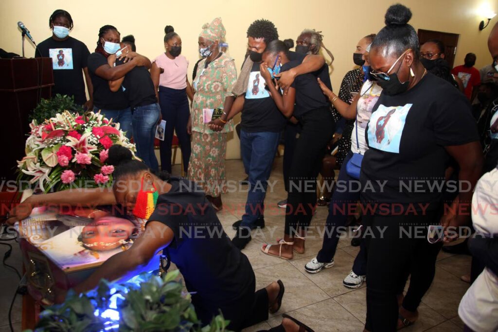 Patrice Cudjoe mother of murdered Keithisha Cudjoe whose body was discovered in the Heights of Aripo, holds on to her casket during her funeral at Dennie's Funeral Home in Belmont, as friends and relatives look on, Thursday. - SUREASH CHOLAI
