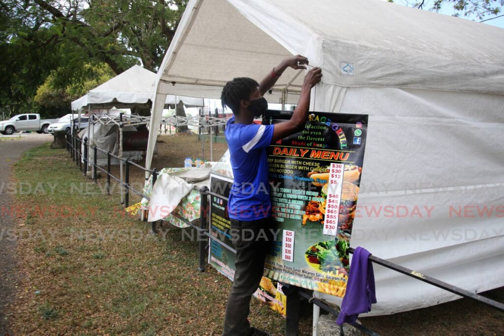 Kwesi Charles fixes a sign on his food stall east of the entrance to the Queen's Park Savannah, Port of Spain where food vendors relocated to Saturday, to allow an easy flow into the safe zone Carnival City. - PHOTO BY SUREASH CHOLAI