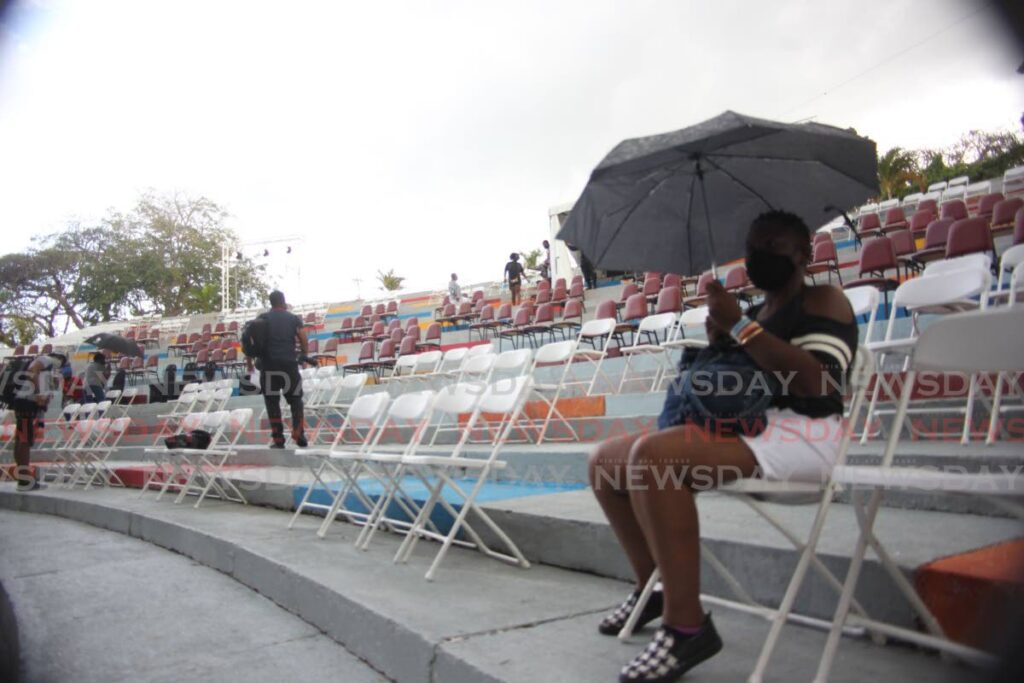 A spectator shelters from a light shower during a calypso show at Naparima Bowl, San Fernando last Sunday. An adverse weather alert has been discontinued. - Photo by Lincoln Holder