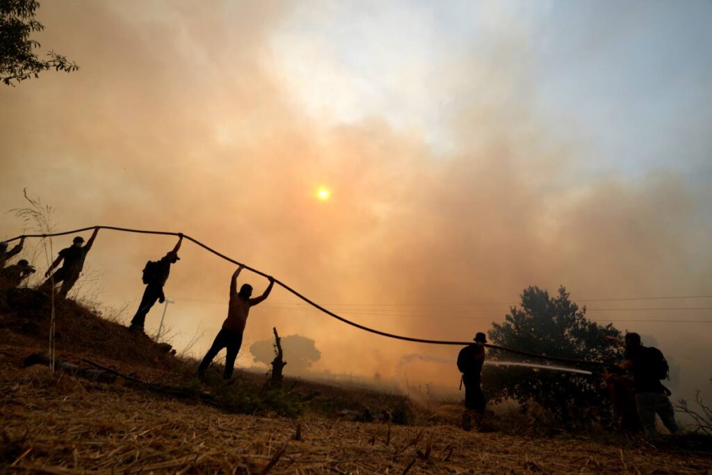 A firefighter tries to extinguish a fire as volunteers hold the water hose during a wildfire in Agios Stefanos, in northern Athens, Greece, on August 6, 2021. - AP PHOTO