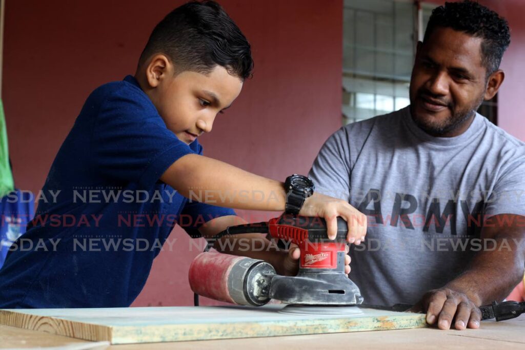 In this file photo, Under the careful watch of his father Elkin Matute, Bejamin sands a piece of wood at the carpentry workshop at the family home in Diego Martin. - PHOTO BY ROGER JACOB