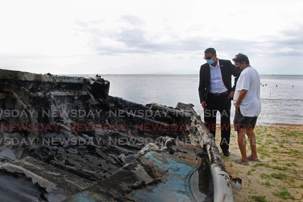 Couva North MP Ravi Ratiram and president of the Carli Bay fishing association Imtiaz Khan look at one of the burnt boats on Tuesday. - Marvin Hamilton