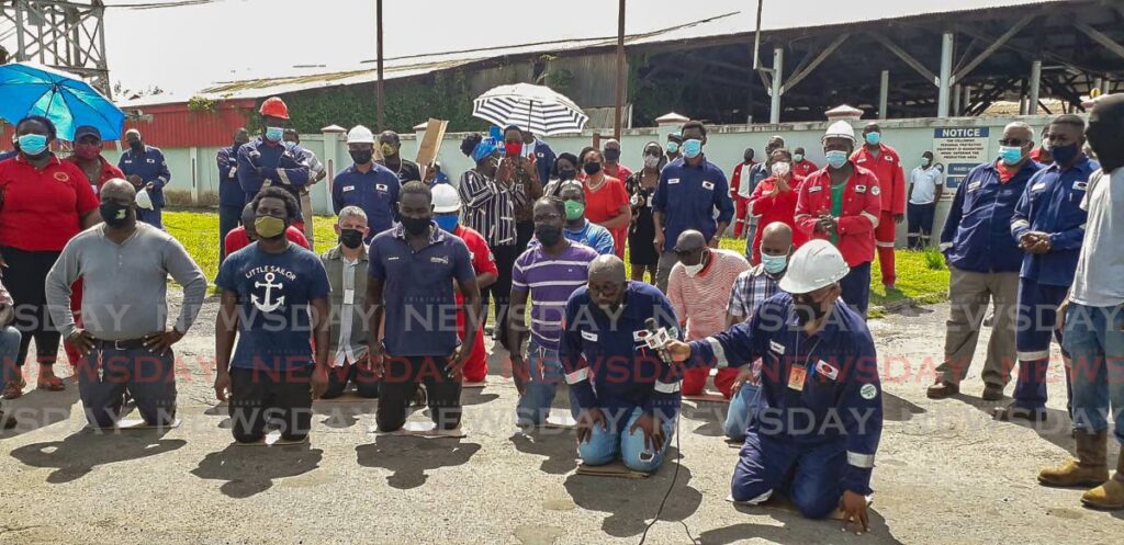 Lake Asphalt workers kneel in front the company's gates in September last year as they called on government to intervene to ensure their salaries were paid. - 