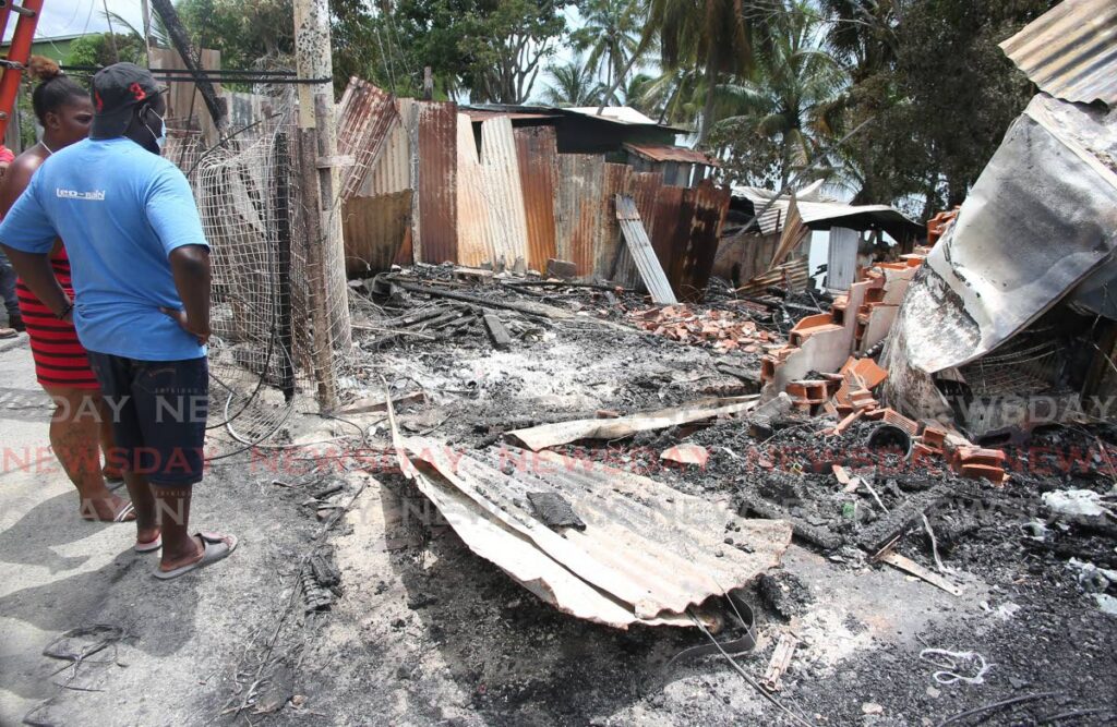 Fire victim Junior John and a neighbour look at the burnt the remains after fire that destroyed his home and two other structures on Bay road, Marabella on Thursday night. Photo by Lincoln Holder
