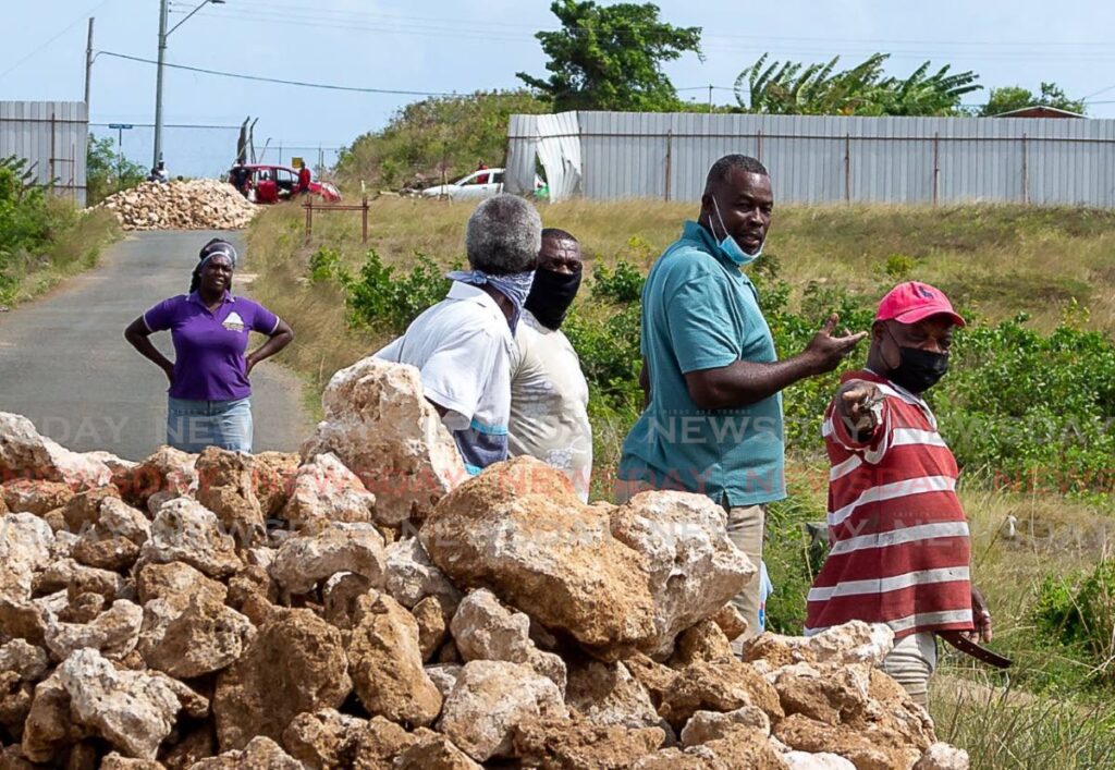 Residents of Silk Cotton Trace and Crompston Trace, Crown Point, ponder their next move as China Railway Construction workers left boulders in the roadway leading to their homes on Friday. - DAVID REID