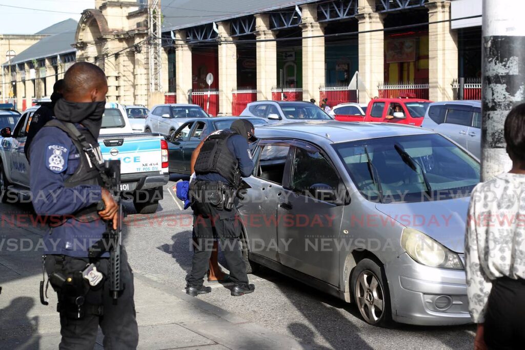 A police officer speaks to the driver of a car that was shot at by unidentified gunmen in downtown Port of Spain on Monday near City Gate on South Quay. Photo by Roger Jacob