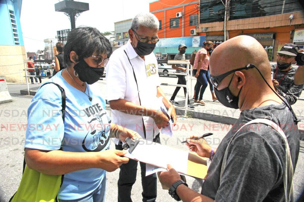 David Abdulah, leader of the Movement for Social Justice, centre, looks on as Shaheed Moammed, right, signs a petition against high food and fuel prices presented by a member of Trinbagonians Drive for Progress at Library Corner, San Fernando. - LINCOLN HOLDER