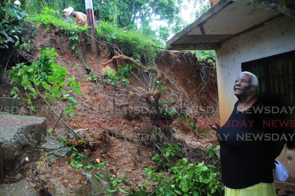 T&TEC workers, at the top, stabilise an electricity pole to prevent it from falling on Martha Alleyne's, right, house after it was dislodged by a landslide during heavy rainfall on Tuesday night at Second Caledonia, Morvant. - SUREASH CHOLAI