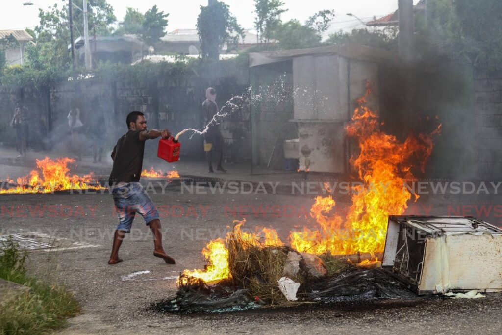 A resident of Sea Lots throws fuel on burning debris during a protest on Monday over the killing of a man and two teen boys by police in Port of Spain on Saturday morning. - ANGELO MARCELLE