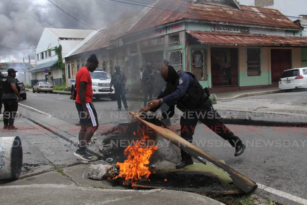 A policeman tries to put out a fire on Nelson Street, Port of Spain during protests by residents over the killing of three men by police at Independence Square, Port of Spain on Saturday. Photo by Ayanna Kinsale 