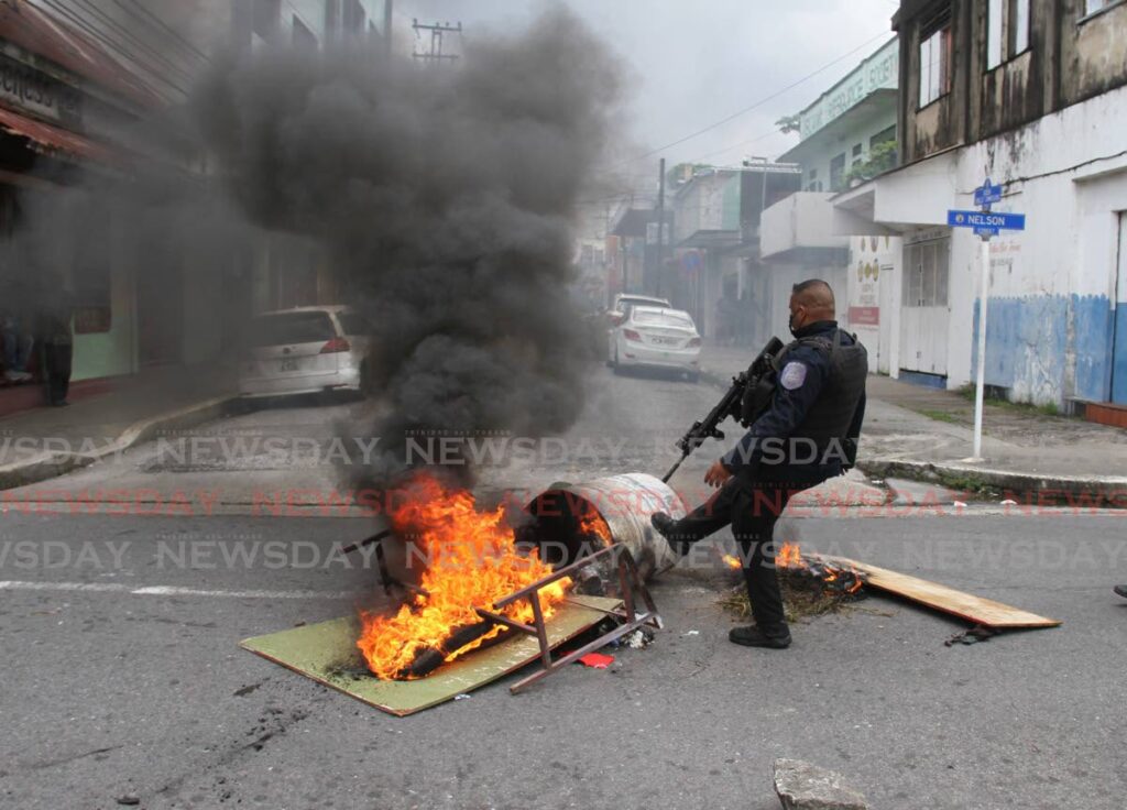 CLEARING THE WAY: A policeman removes burning debris from Nelson Street, Port of Spain after protests over the police-involved killings of three men on the weekend. PHOTO BY AYANNA KINSALE
