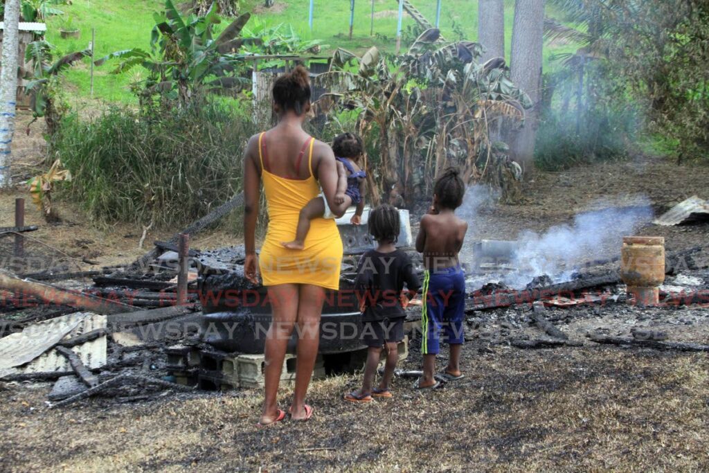 Sequoia St George and her three children, watch the burnt remains of their Pond Street, Point Fortin home on Thursday.  Photo by Angelo Marcelle