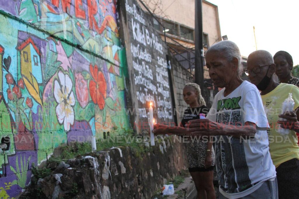 Precilla Brooks, mother of Noel Diamond, one of three men killed by police two years ago at Juman Drive, 2nd Caledonia, places a candle at the site of the men's death on Tuesday. Earlier, eight policemen appeared in court charged with the men's murders. - Angelo Marcelle