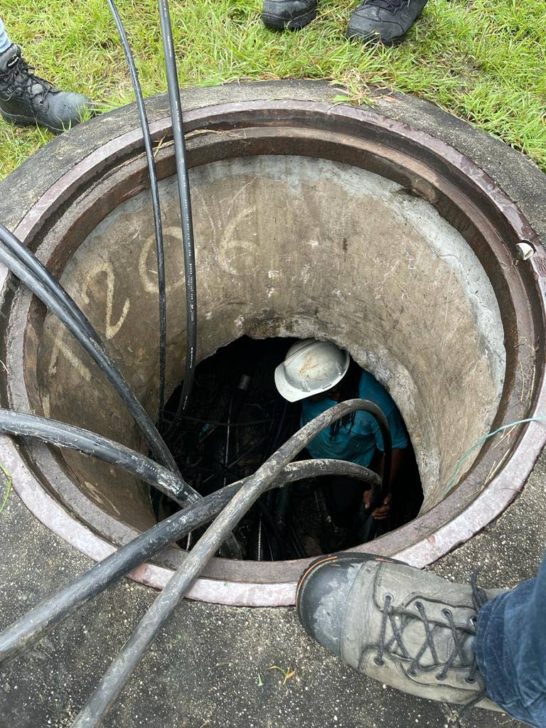 TSTT workmen inspect the vandalised cables in its underground installation on Sunday. PHOTO COURTESY TSTT - TSTT